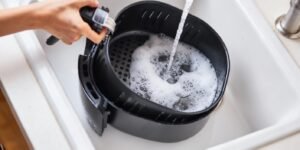 Persona limpiando una Air Fryer FOXBOX Aeris 6000 NV con esponja suave sobre mesada de cocina argentina.